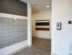 Interior of a modern building hallway featuring a wall of gray mailboxes, a colorful abstract painting, and a digital thermostat.