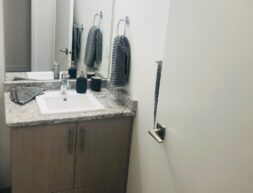 A modern bathroom featuring a single vanity with a granite countertop, two pendant lights, and neatly hung gray towels.