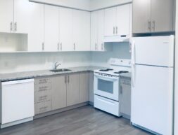 A modern kitchen with white cabinets, granite countertops, and stainless steel appliances, including a dishwasher, stove, and refrigerator.