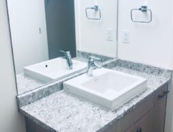 A modern bathroom vanity featuring two rectangular sinks, granite countertop, and wall-mounted mirrors with sconce lighting.