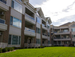 Modern residential apartment buildings with balconies, large windows, and a manicured lawn under a clear sky.