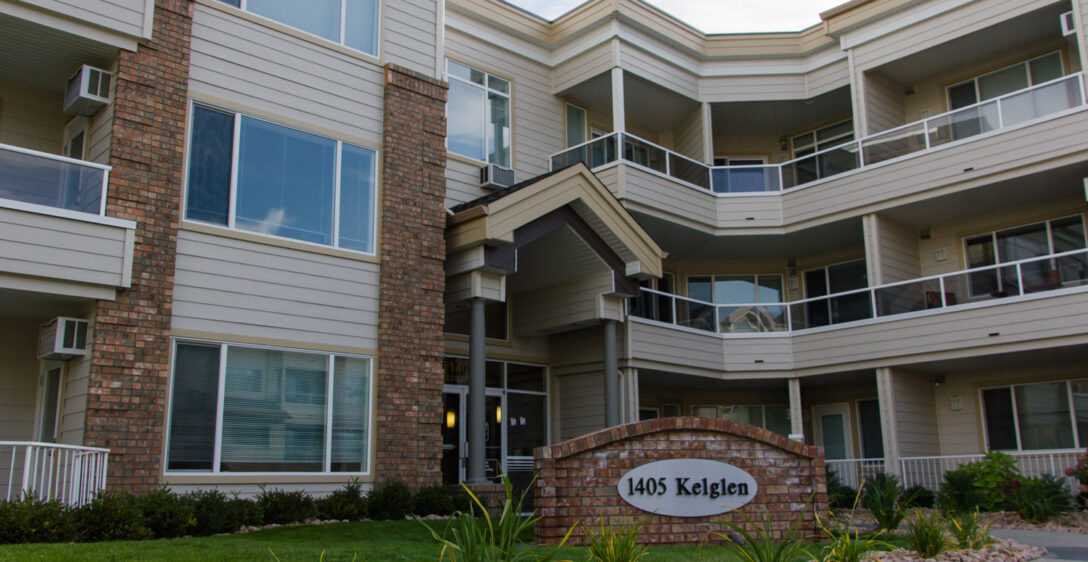 Exterior of a modern apartment building with multiple balconies, a brick facade, and a sign reading "1405 keglen" at the entrance.