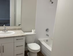 A modern bathroom with a white toilet, sink with vanity, and a bathtub with a glass door.
