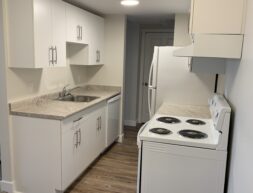 A small modern kitchen with white cabinets, gray countertops, a sink, an electric stove, and a refrigerator.